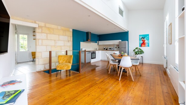 A modern kitchen with white cabinets, a dining area with wooden chairs, and a large window providing natural light.