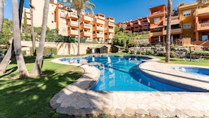 A swimming pool surrounded by stone tiles, palm trees, and multi-story buildings with balconies. - Apartment 'Reserva Marbella' with Shared Pool, Wi-Fi and Air Conditioning (Marbella)