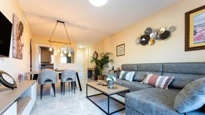 A living room with a grey sofa, a coffee table, and a dining area with chairs. - Apartment 'Reserva Marbella' with Shared Pool, Wi-Fi and Air Conditioning (Marbella)