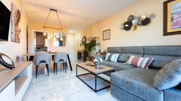 A living room with a grey sofa, a coffee table, and a dining area with chairs.