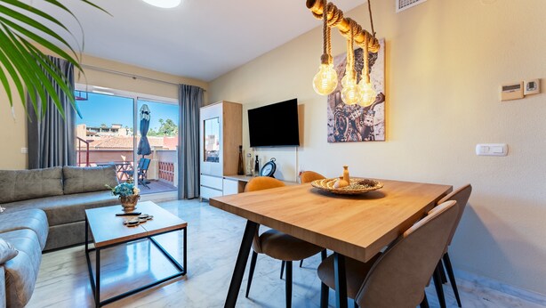 A modern living room with a sofa, coffee table, dining table with chairs, a TV, and a large window with a view. - Apartment 'Reserva Marbella' with Shared Pool, Wi-Fi and Air Conditioning (Marbella)