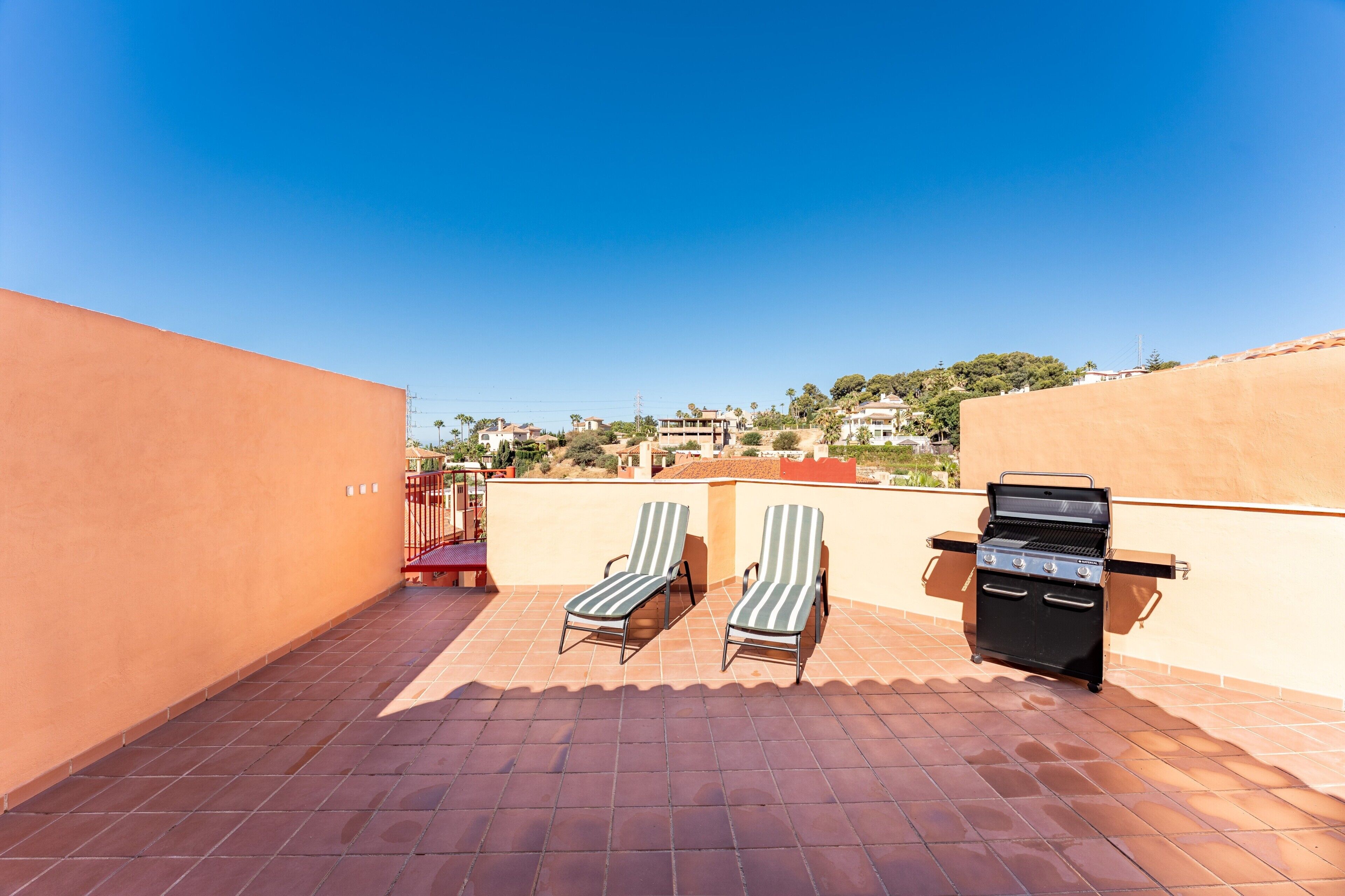 Une terrasse sur le toit, dotée de deux chaises longues à rayures, d’un barbecue et offrant une vue dégagée sur le paysage urbain.