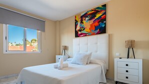 A bedroom with a bed, a nightstand, a lamp, a painting, and a window with a view. - Apartment 'Reserva Marbella' with Shared Pool, Wi-Fi and Air Conditioning (Marbella)