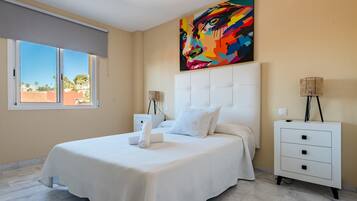 A bedroom with a bed, a nightstand, a lamp, a painting, and a window with a view.