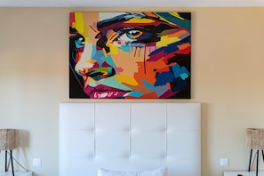 Une pièce avec un grand tableau abstrait aux couleurs vives accroché au mur, une tête de lit capitonnée et deux lampadaires.