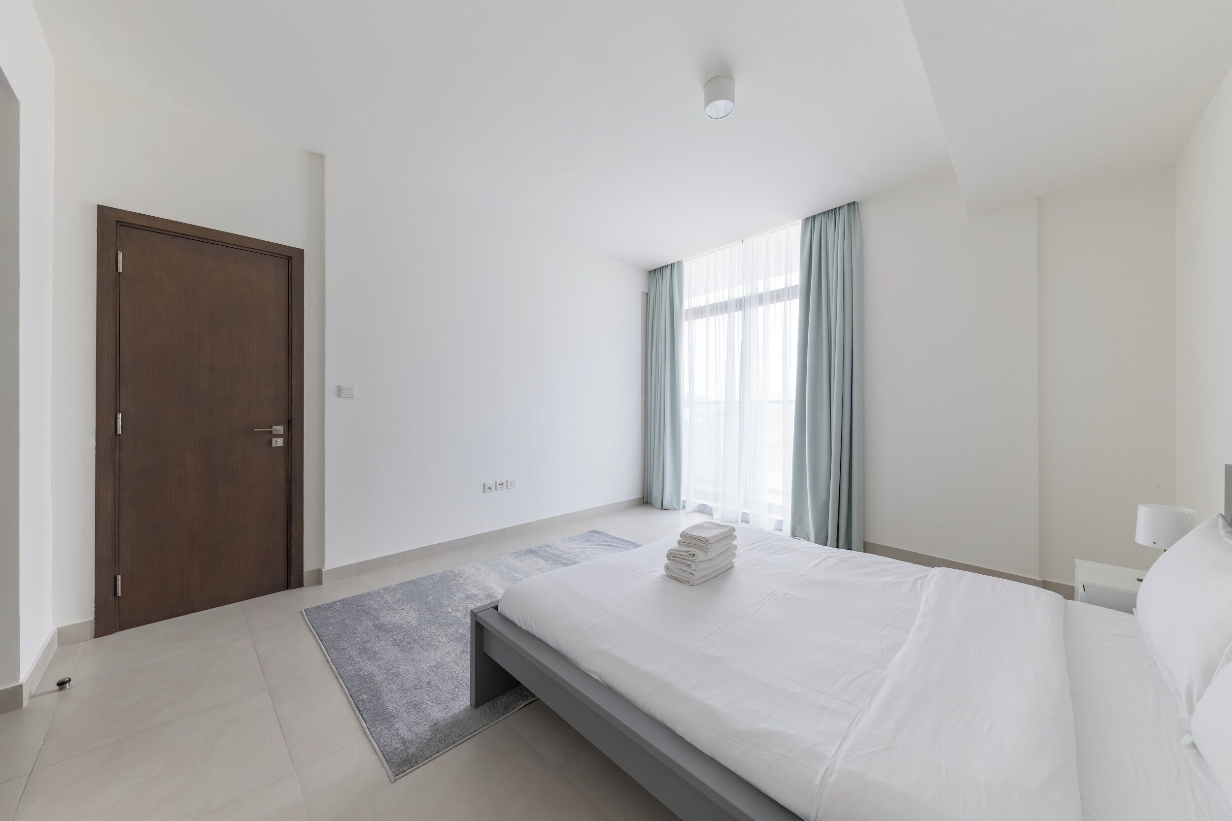 A modern hotel room with a bed, a door, and a window with curtains.