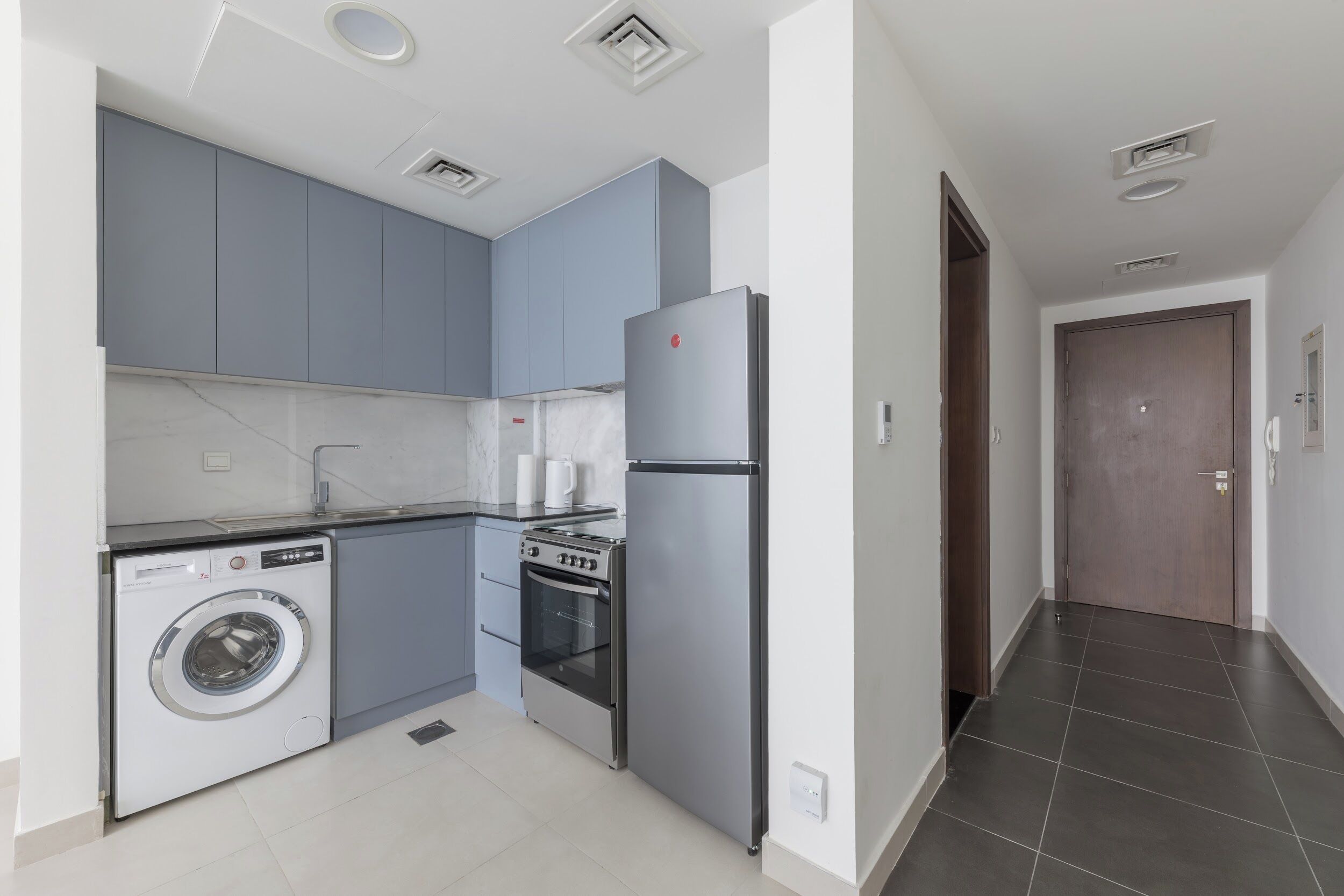 Une cuisine moderne avec des meubles gris, un réfrigérateur en acier inoxydable, un lave-linge et un four.