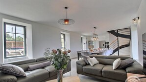 A modern living room with two sofas, a coffee table, and a vase of flowers. There is a dining area in the background with a staircase leading to an upper level. - Kergonet - Plougrescant (PLOUGRESCANT)