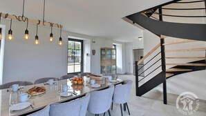 A modern dining area with a long table, chairs, and hanging light fixtures. A spiral staircase is visible to the right. - Kergonet - Plougrescant (PLOUGRESCANT)
