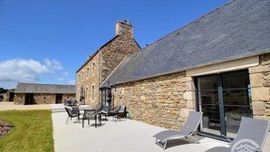 A stone building with a thatched roof, outdoor seating area with chairs and tables, and a clear sky. - Kergonet - Plougrescant (PLOUGRESCANT)