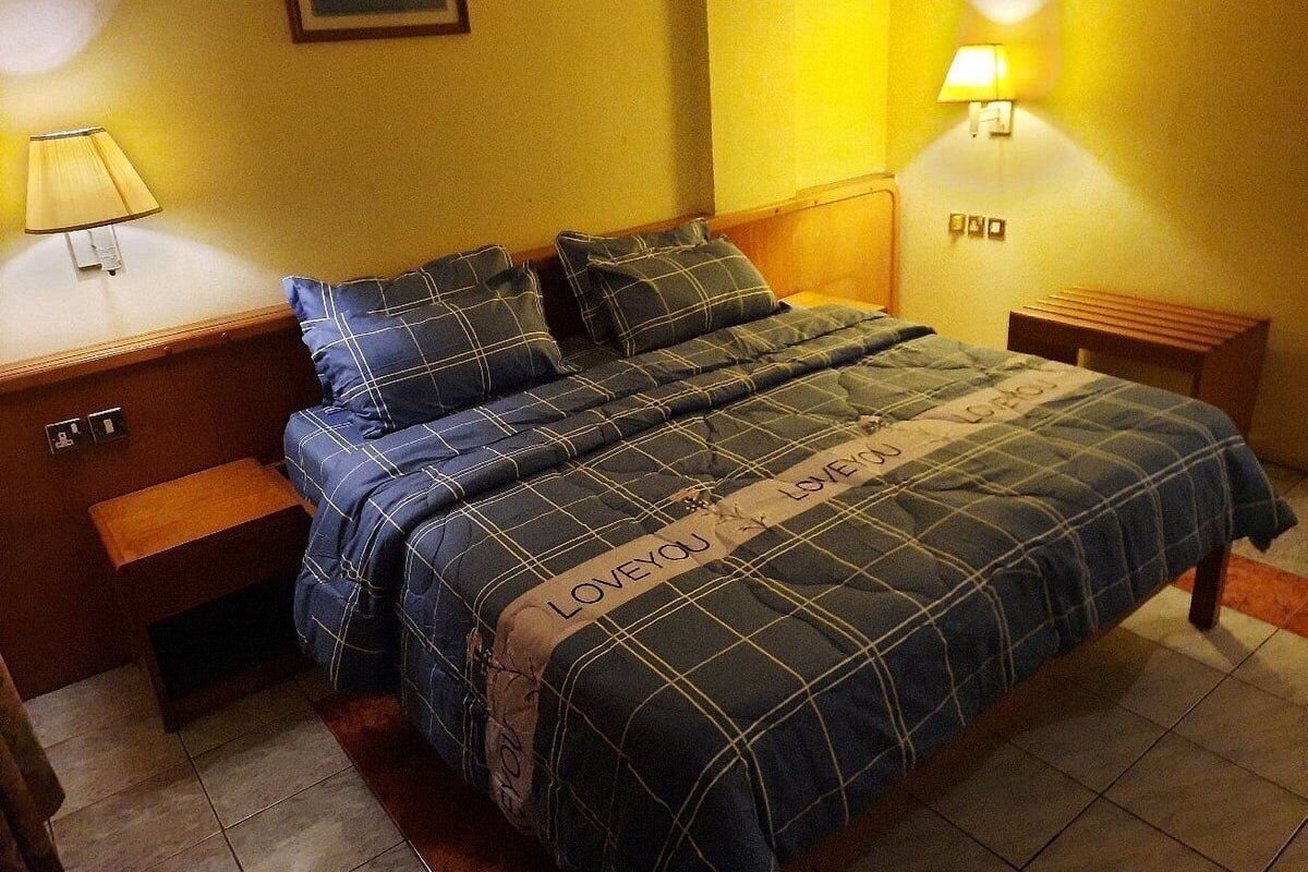 A bed with a plaid bedspread and pillows, a bedside table with a lamp, and a wall-mounted light fixture.