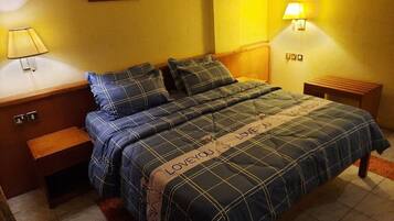 Una cama con colcha y almohadas a cuadros, una mesita de noche con lámpara, y un aplique de pared.