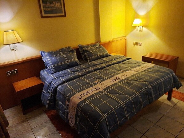 A bed with a plaid bedspread and pillows, a bedside table with a lamp, and a wall-mounted light fixture.