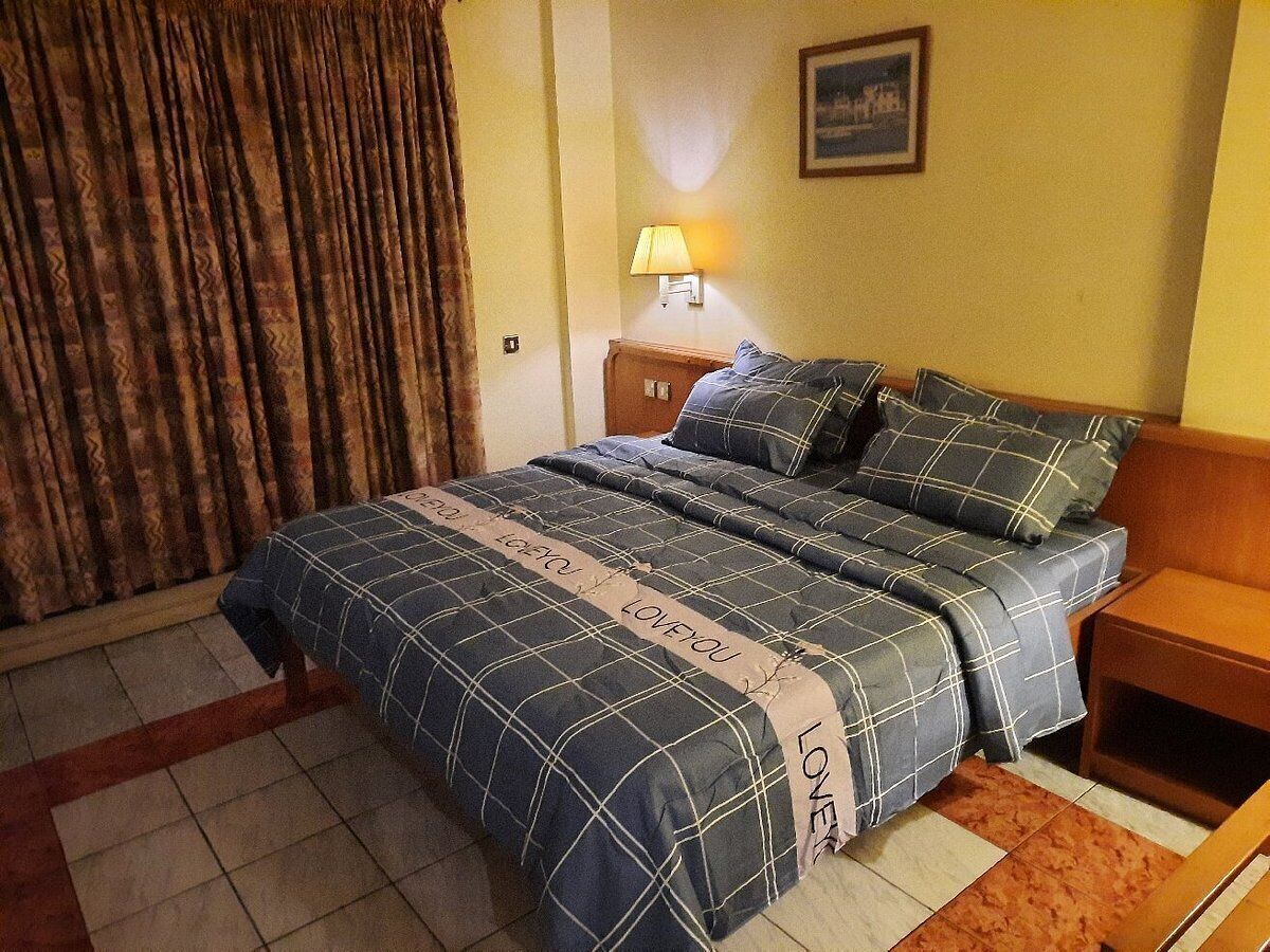 A hotel room with a bed, a nightstand, a lamp, and a curtain.