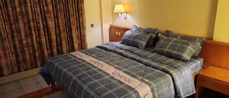 A hotel room with a bed, a nightstand, a lamp, and a curtain.