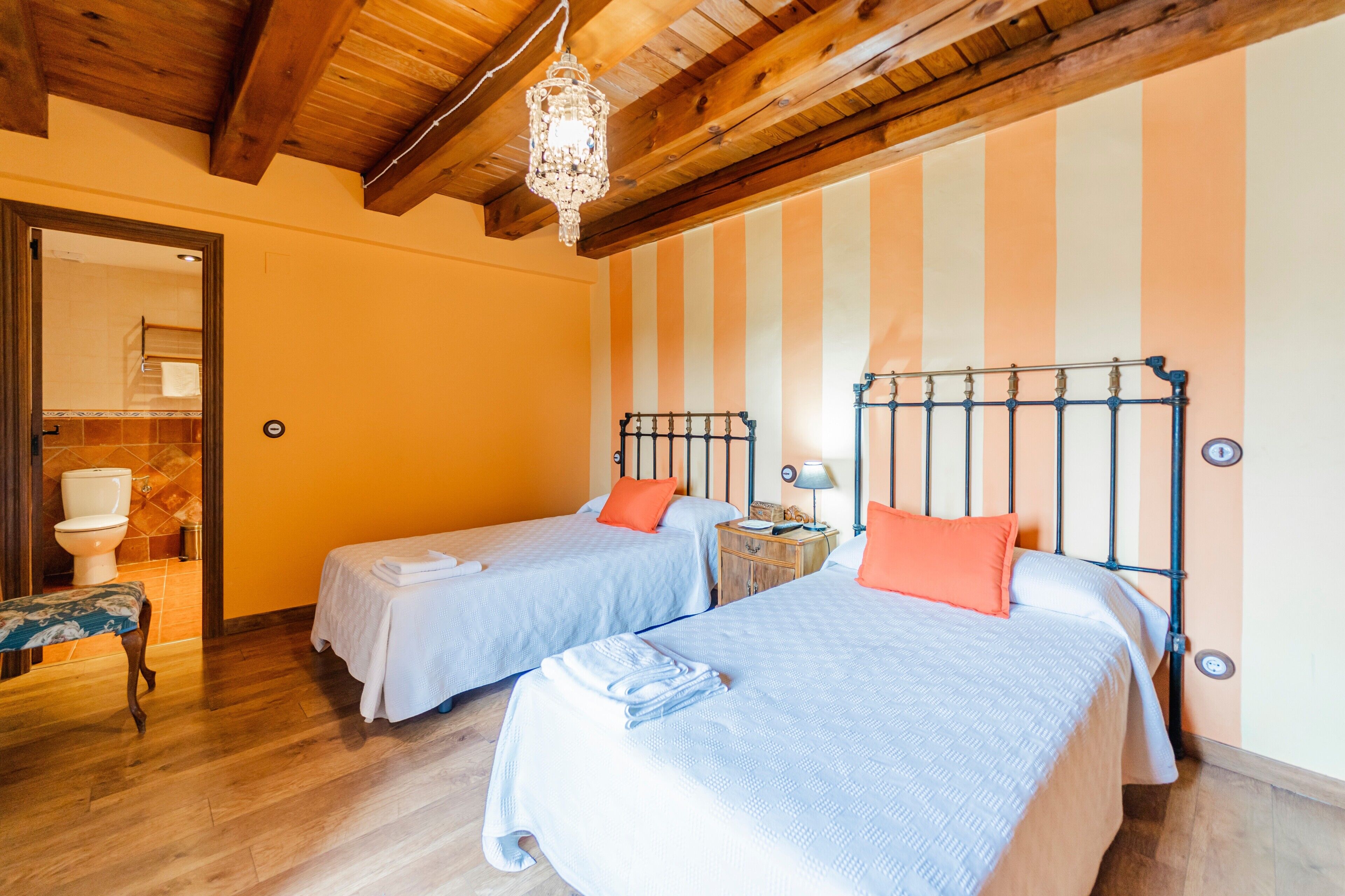 Een kamer met twee bedden, houten vloeren, een kroonluchter en een gestreept behang.