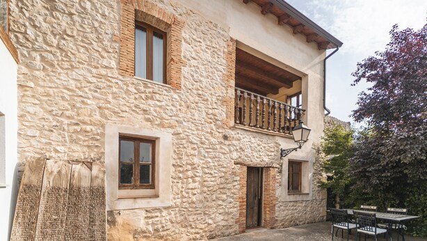 Un bâtiment en pierre doté d’un balcon, d’une porte et d’une table avec des chaises à l’extérieur.