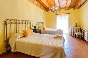 A bedroom with two beds, a nightstand, a table with a vase, and a chandelier.