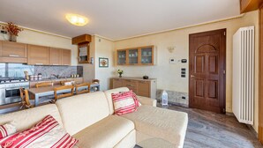 A living room with a sofa, a dining table, and a kitchen area with cabinets and appliances. - Happy Villa Apartment with Lake View, Private Terrace and Wi-Fi (San Felice del Benaco)