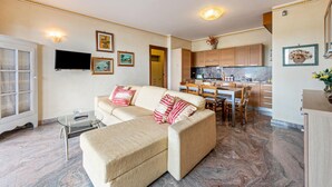 A living room with a sofa, a TV, and a dining area with a table and chairs. - Happy Villa Apartment with Lake View, Private Terrace and Wi-Fi (San Felice del Benaco)
