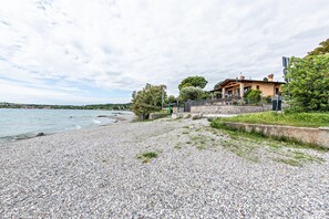 A coastal property with a pebble beach, a stone wall, and a house with a balcony overlooking the sea.