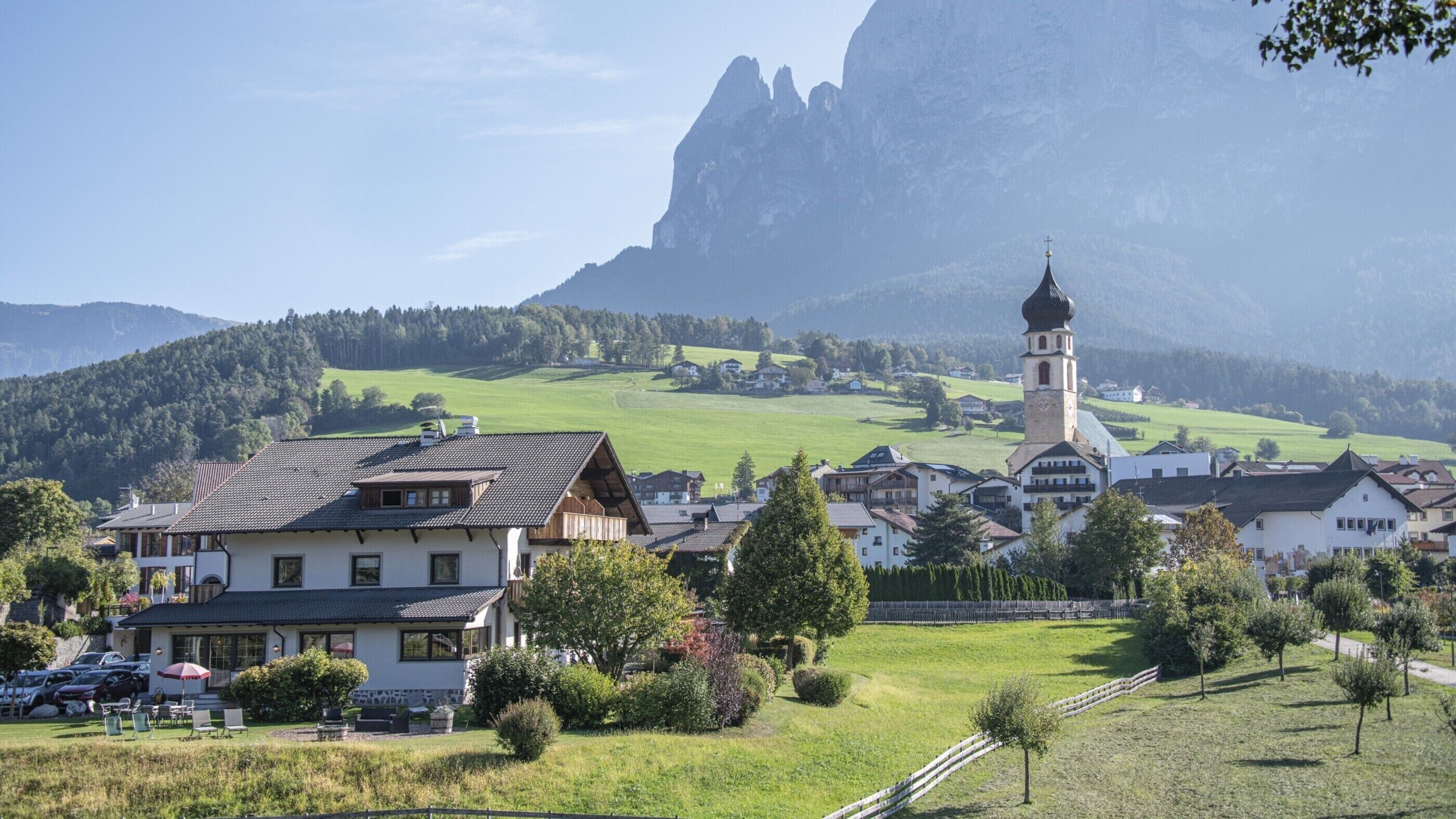 A rural village with traditional architecture, a prominent church tower, and a mountainous backdrop.