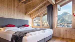 Un dormitorio de cabaña de madera con una cama, dos almohadas, una ventana con vistas a las montañas y un balcón.