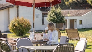 An outdoor seating area with tables and chairs, a red umbrella, and a white building in the background.