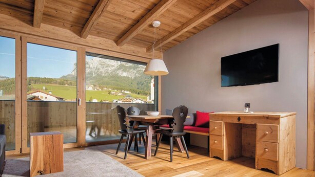 A room with a wooden ceiling, a dining table with chairs, a sofa, a desk with drawers, a television mounted on the wall, and a large window with a view of mountains and houses. - Apartment 'Aparment Family 6' with Mountain View, Shared Garden and Wi-Fi (Fié allo Sciliar)