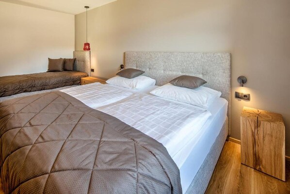 Ein Doppelbett mit grauem Kopfteil, ein Nachttisch und ein Beistelltisch mit Lampe.