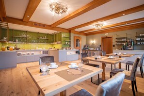 Ein geräumiger Essbereich mit Holztischen und -stühlen, eine Küche mit grünen Schränken und eine Kandelaber.