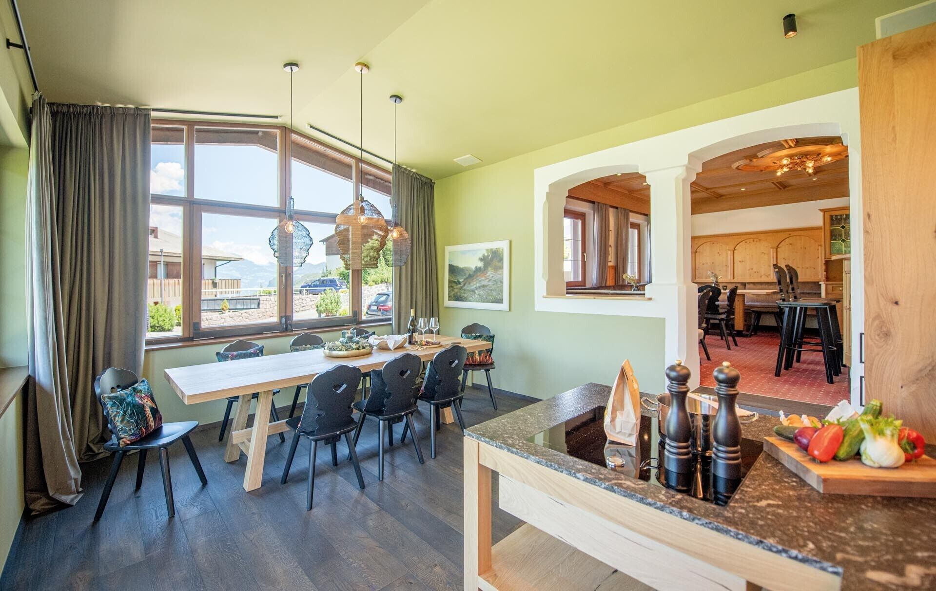 A dining area with a table set for four, a kitchen with a wooden countertop, and a view of the outdoors through large windows.