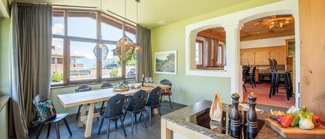 A dining area with a table set for four, a kitchen with a wooden countertop, and a view of the outdoors through large windows.