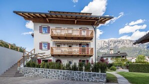 A multi-story building with balconies, a stone staircase, and a mountain backdrop. - Apartment 'Aparment Family 6' with Mountain View, Shared Garden and Wi-Fi (Fié allo Sciliar)