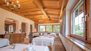 A dining area with multiple tables, wooden ceiling beams, and large windows with a view of greenery. - Apartment 'Aparment Family 6' with Mountain View, Shared Garden and Wi-Fi (Fié allo Sciliar)
