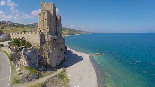 Un castillo costero con una playa y mar azul cristalino.