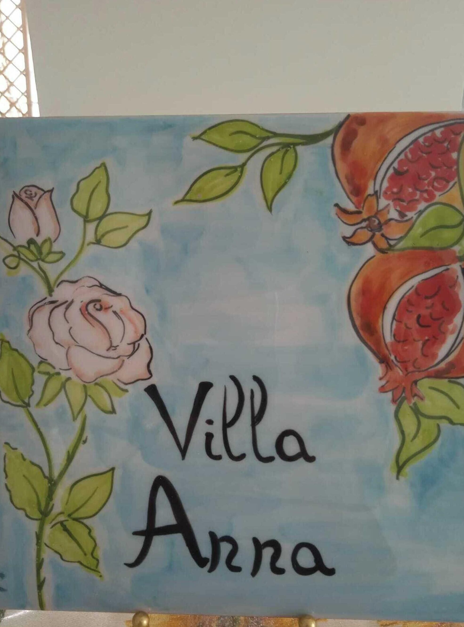 Un senyal decoratiu amb el nom 'Villa Anna' envoltat d'il·lustracions d'una rosa i una melgranada.