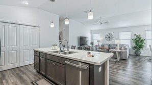 Une cuisine moderne dotée d’un îlot central, d’appareils électroménagers en acier inoxydable et de luminaires suspendus.