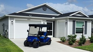 Une maison moderne à deux étages, avec un garage, une voiturette de golf bleue garée devant et une pelouse bien entretenue.