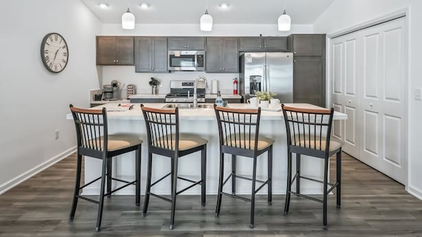 Une cuisine moderne dotée d’un îlot central, d’appareils électroménagers en acier inoxydable et de luminaires suspendus.