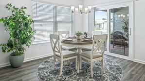 Un coin repas avec une table ronde, des chaises blanches, un lustre et une plante en pot.