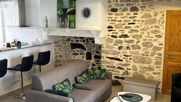 Een gezellige woonkamer met een stenen muur, een open haard, een bank en een eethoek met stoelen.