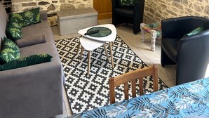 A stone-walled room with a wooden door, a television mounted on the wall, a sofa, a chair, and a small table with a remote control. - Charming Fitness & Wellness Gîte with Shared Pool (Masseret)