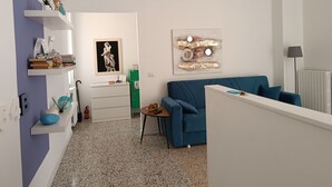 A modern living room with a blue sofa, a small table with a bowl of fruit, a white fireplace, and a green radiator. - 64B 10 minutes walk from: Polyclinic Hospital, Station and Center - 2 rooms (Pavia)