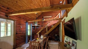 Interior rústico de uma cabana de madeira, com área de jantar, televisão e um letreiro escrito 'ANTIQUE'.