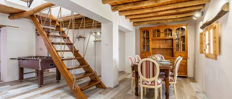 Un escalier en bois, une table à manger avec des chaises et un buffet en bois dans une pièce dont le sol et le plafond sont également en bois, ce dernier étant incliné.