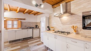 A modern kitchen with wooden beams, a gas stove, and white cabinetry. - Holiday Home "Casa Rústica – Your Retreat with Terrace and Mountain Views" (Vélez de Benaudalla)
