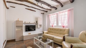 A living room with a sofa, a glass coffee table, a TV, and wooden beams on the ceiling. - Holiday Home "Casa Rústica – Your Retreat with Terrace and Mountain Views" (Vélez de Benaudalla)