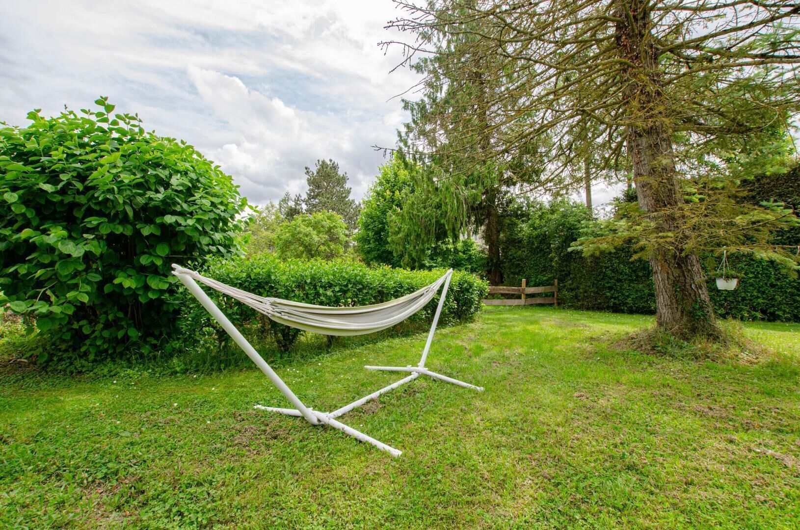 A hammock in a grassy garden with trees and a wooden fence in the background.