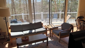 Un salon comprenant un canapé, des fauteuils, une table basse et un téléviseur. Il y a un balcon avec une balustrade et du mobilier d’extérieur.
